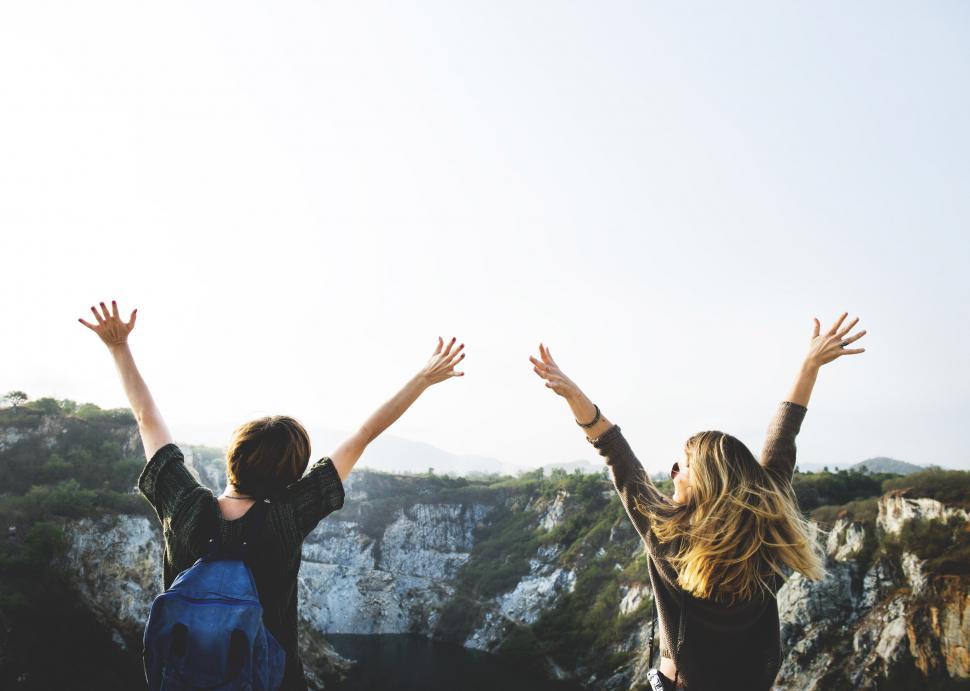 zwei weiße Frauen wandern auf dem Gipfel eines Berges und posieren mit erhobenen Armen an einem sonnigen Tag